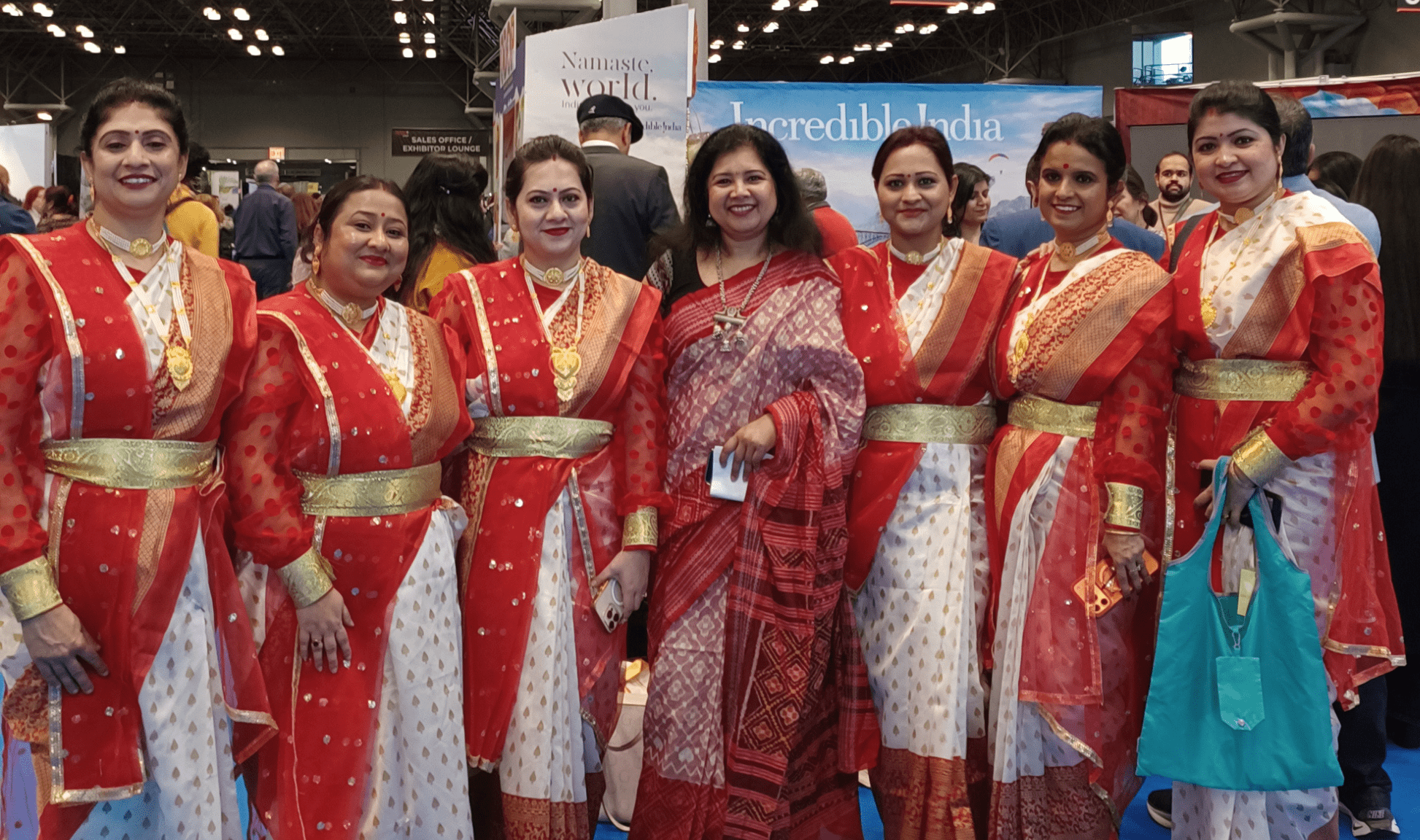 A spotlight performance on the Global Beats Stage at the 2026 New York Travel & Adventure Show. Two dancers perform a traditional Indian classical dance, wearing vibrant orange and red silk costumes with intricate gold jewelry and floral headpieces. The performance was part of the India tourism spotlight at the Javits Center.